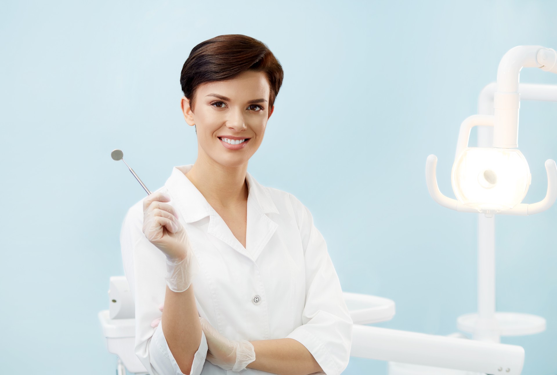 Beautiful smiling woman in white lab coat holding dental mirror.